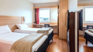 A hotel room with two beds, a desk, a chair, a TV, and a window with a view.