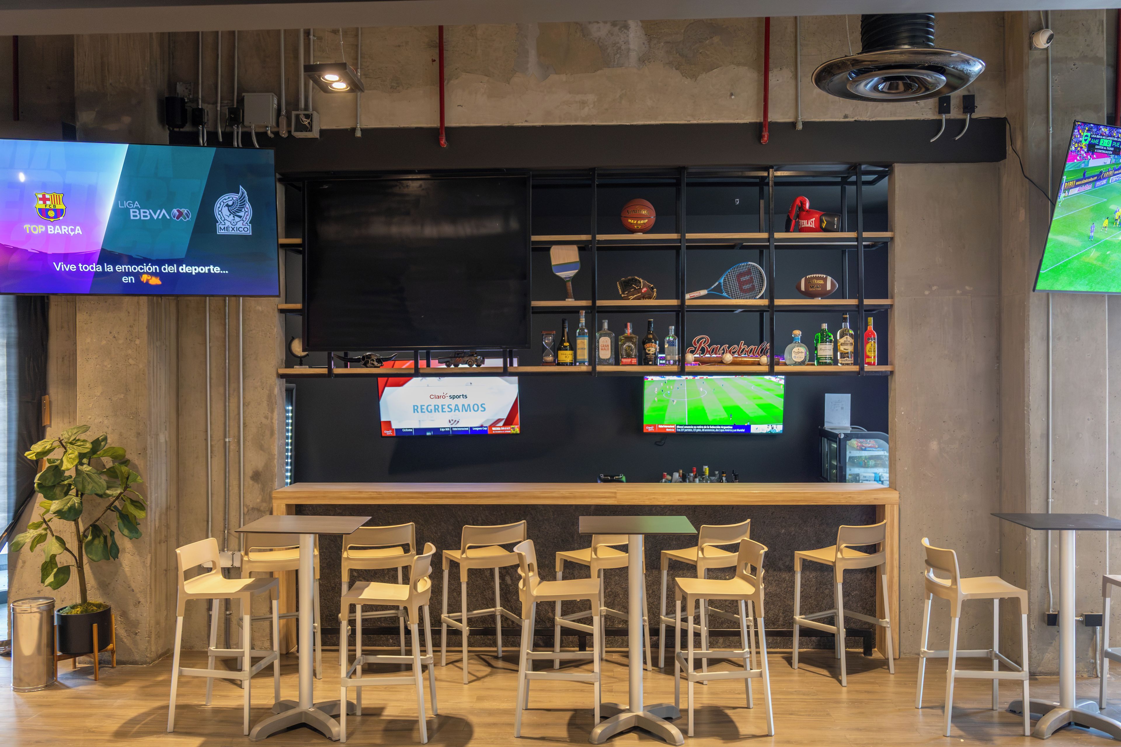 Eine Bar mit verschiedenen Sitzgelegenheiten, einem Fernseher, der Sport zeigt, und Regalen mit unterschiedlichen Artikeln.