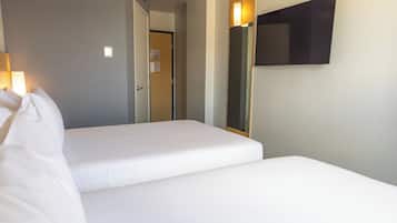 A hotel room with two single beds, a door leading to a hallway, and a wall-mounted TV.