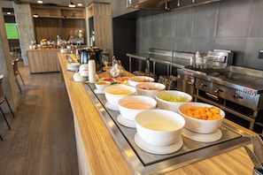A buffet setup with various food items and a commercial kitchen in the background. - ibis Juarez Consulado (Ciudad Juárez)