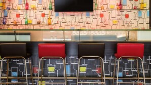 Zona de bar con pared decorativa, televisor de pantalla plana y asientos acolchados rojos.