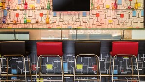 A bar area with a patterned wall, a flat-screen TV, and red cushioned seating.