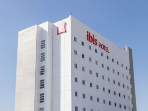 A modern hotel building with a prominent 'ibis HOTEL' sign on the facade.
