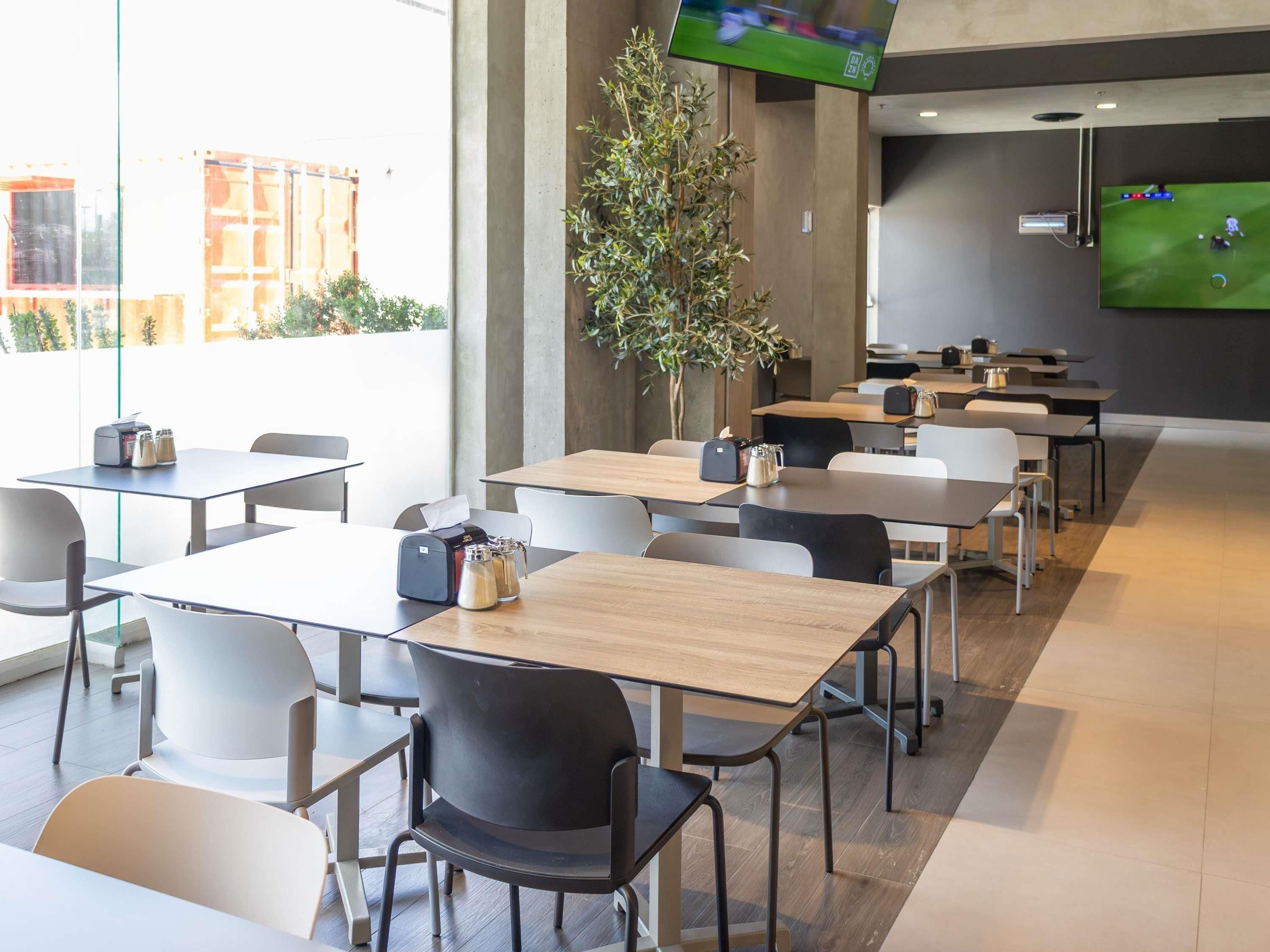 Un espace repas moderne avec des tables et des chaises, un écran de télévision et une plante en pot.