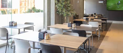 A modern dining area with tables and chairs, a television screen, and a potted plant.