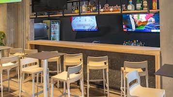 Zona de bar con barra, asientos y una pantalla mostrando deportes.