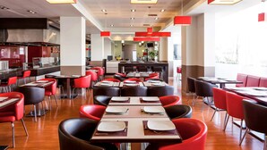 Un restaurante moderno con sillas y mesas rojas, una zona de cocina y un ambiente luminoso.