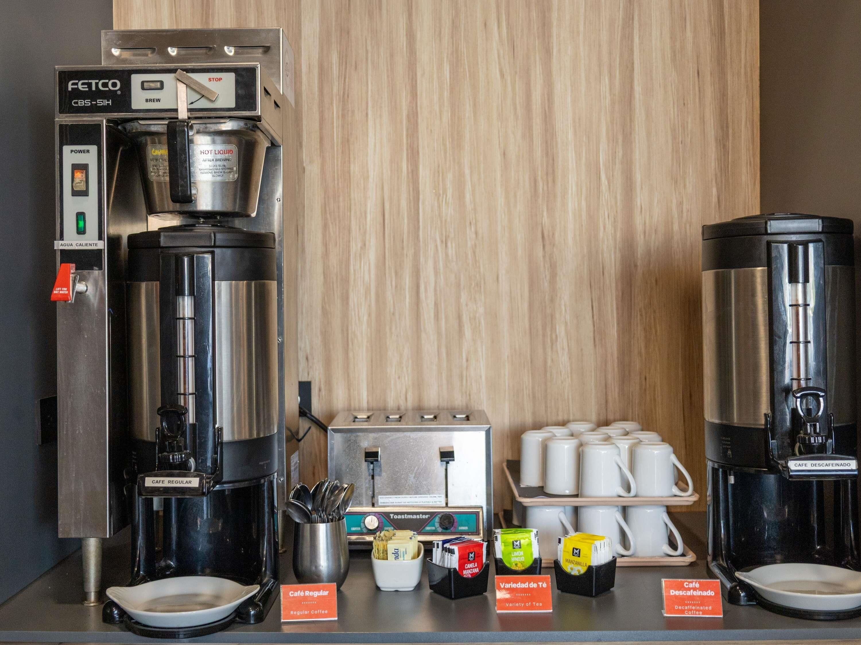 A coffee station with a FETCO CBS-5IH coffee machine, a toaster, and labeled coffee options like 'Café Regular' and 'Variedad de Té'.