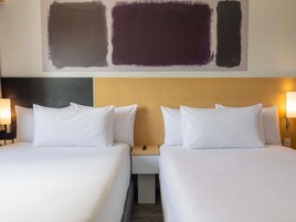 Habitación de hotel con dos camas, cabecero de madera, lámparas de noche y una pared con arte abstracto.