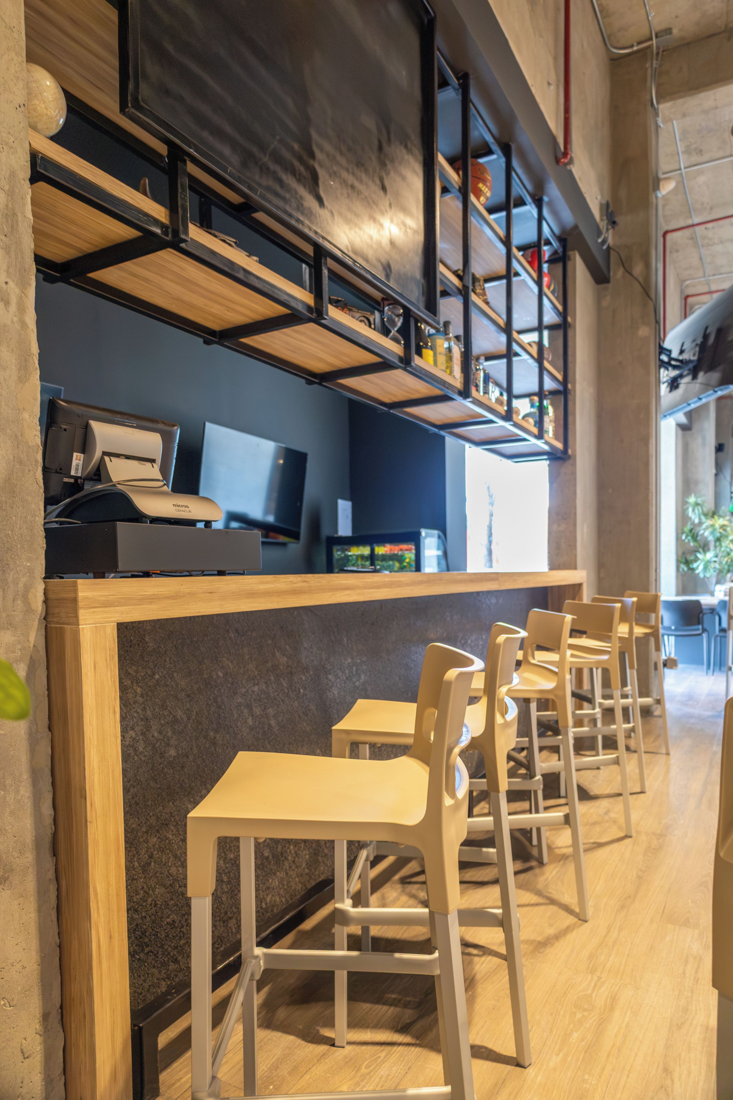 Un interior moderno con mesas y sillas de madera, una barra con una computadora y estanterías arriba.