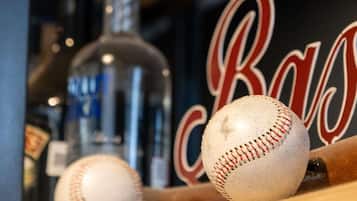 Un bate de béisbol con una pelota y una botella en primer plano, con un fondo borroso que muestra una pared con las letras 'R' y 'B' en rojo y blanco.