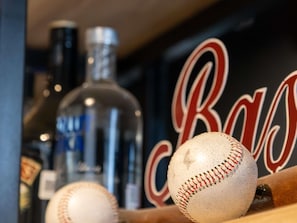 A baseball bat with a ball and a bottle in the foreground, with a blurred background featuring a wall with the letters 'R' and 'B' in red and white.