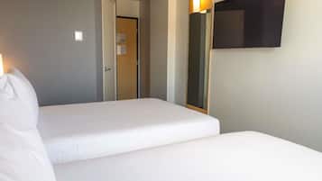 Habitación de hotel con dos camas, un televisor montado en la pared y una puerta que da a otra habitación.