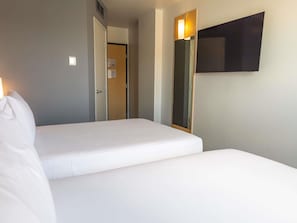 A hotel room with two beds, a television mounted on the wall, and a door leading to another room.