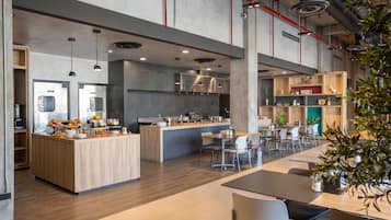 Cocina moderna y amplia con una isla central, comedor con mesas y sillas, y electrodomésticos a la vista.