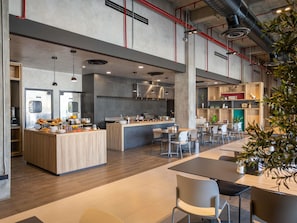 A spacious modern kitchen with a central island, dining area with tables and chairs, and visible kitchen equipment.