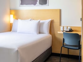 Habitación de hotel con cama, almohadas, escritorio con silla, teléfono y una lámpara de pared.