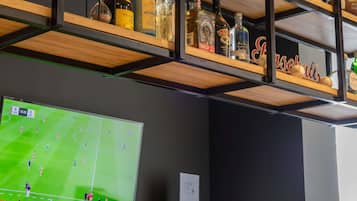 Eine Barbereick mit Regalen voller Spirituosenflaschen und einem Fernseher, der ein Fußballspiel zeigt.