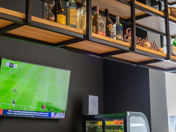 A bar area with shelves holding liquor bottles and a television displaying a soccer match.
