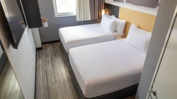 Habitación de hotel con dos camas, piso de madera, una ventana con cortinas y una mesita de noche con lámpara.
