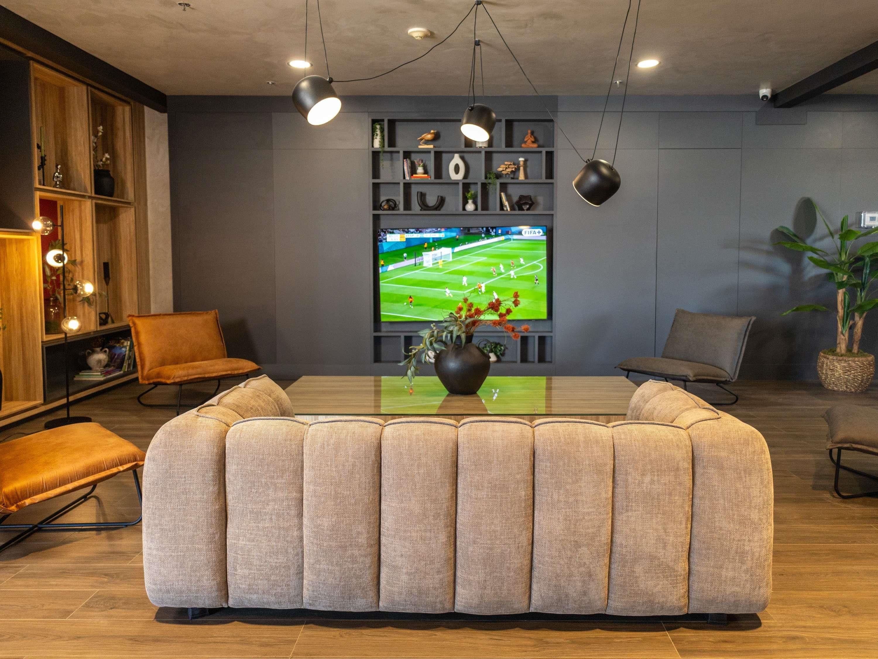 A modern living room with a large sectional sofa, a coffee table, and a television displaying a sports game.
