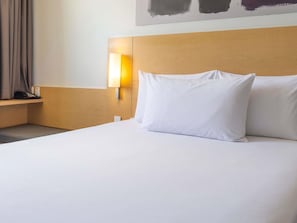 A hotel room with a wooden headboard, a bedside lamp, and a white bed. - ibis Juarez Consulado (Ciudad Juárez)