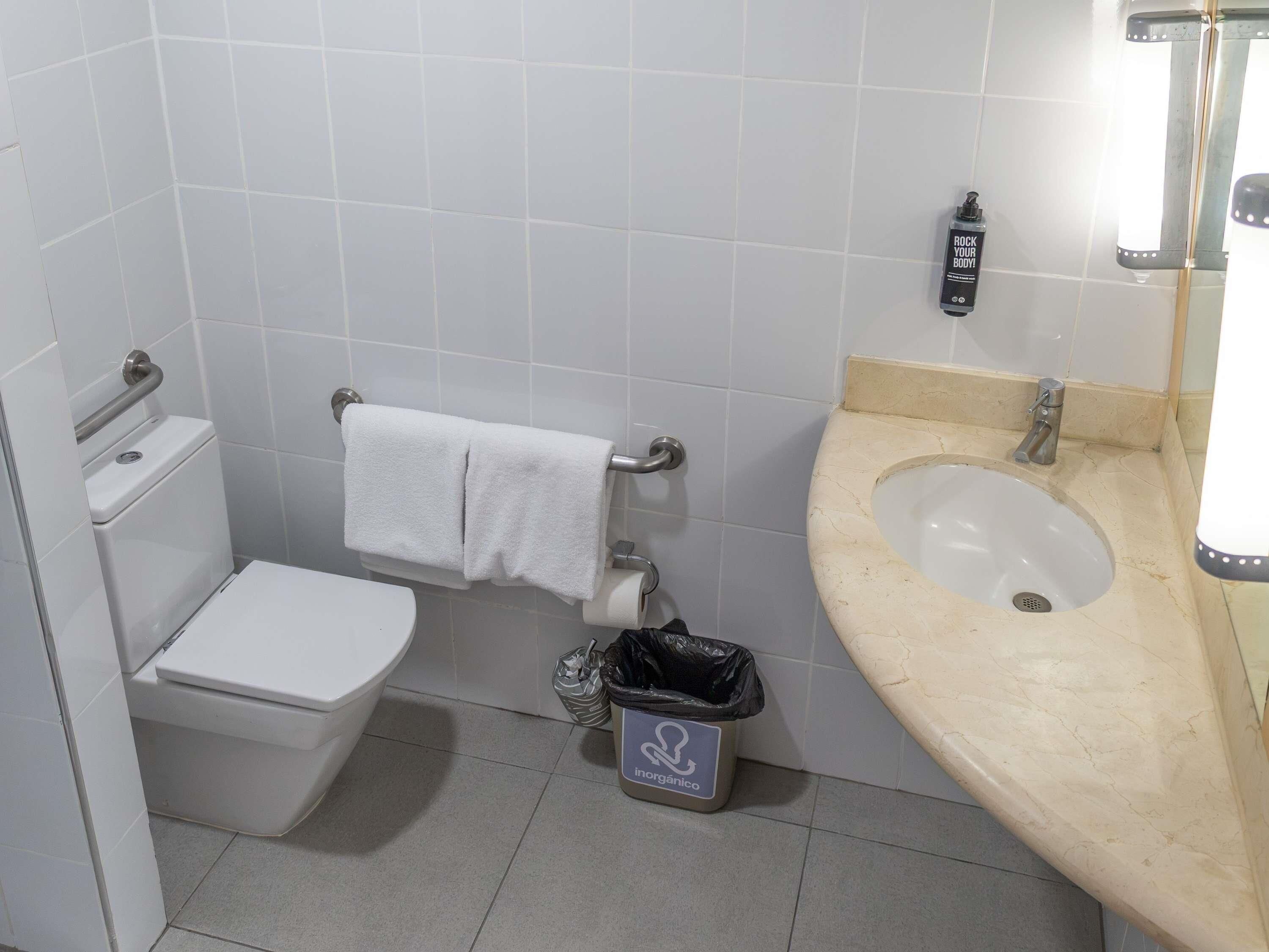 A bathroom with a toilet, a sink, a towel rack, and a trash bin.