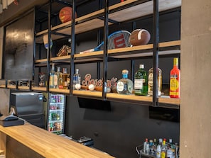 A bar area with shelves displaying sports balls, bottles, and a sign reading 'Baseball'.