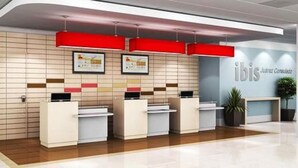 Un área de recepción con diseño moderno, que incluye un mostrador con pantalla digital, certificados enmarcados en la pared y el logotipo de 'ibis'.