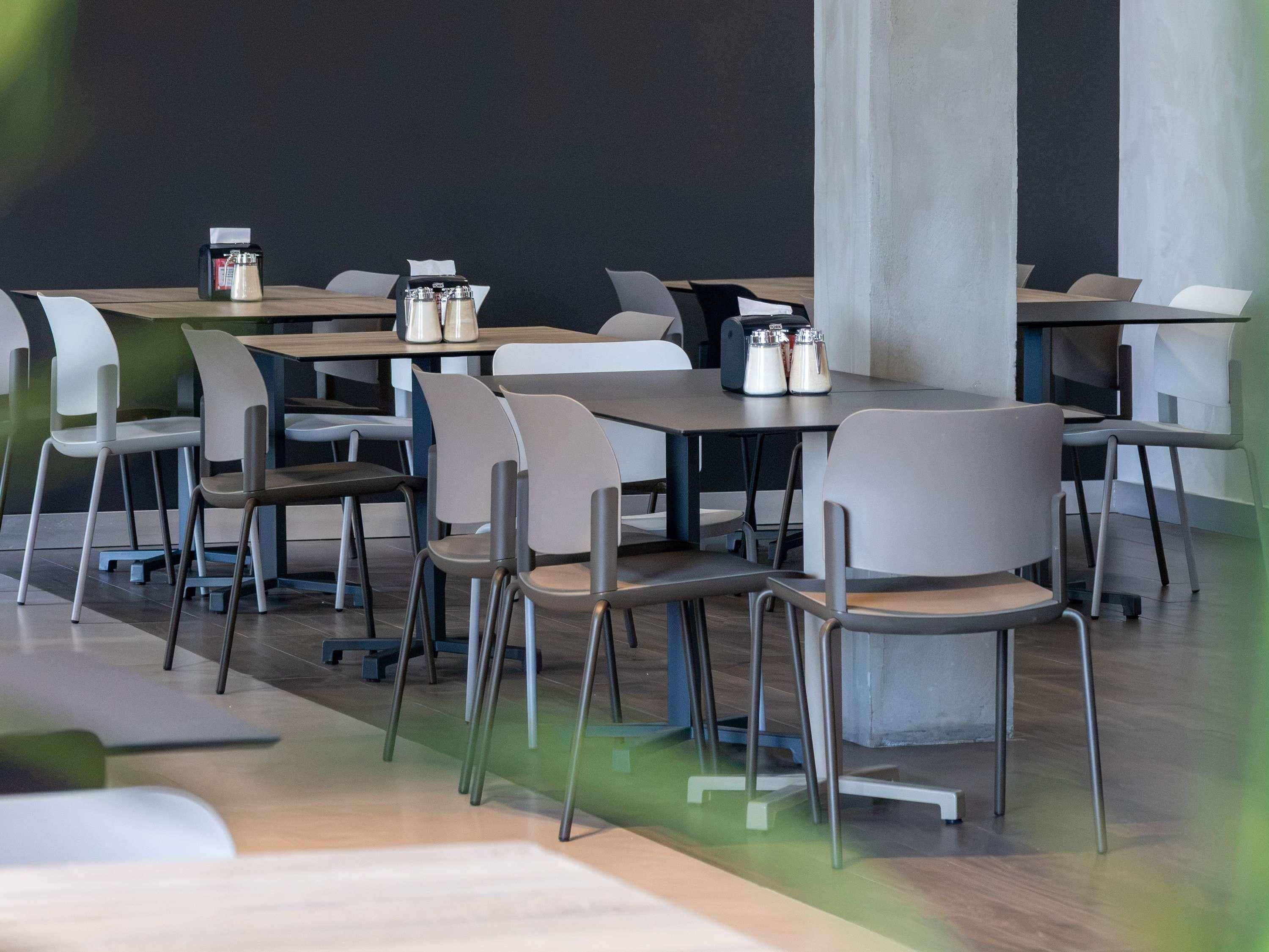 A modern dining area with tables and chairs, some with condiments on them.