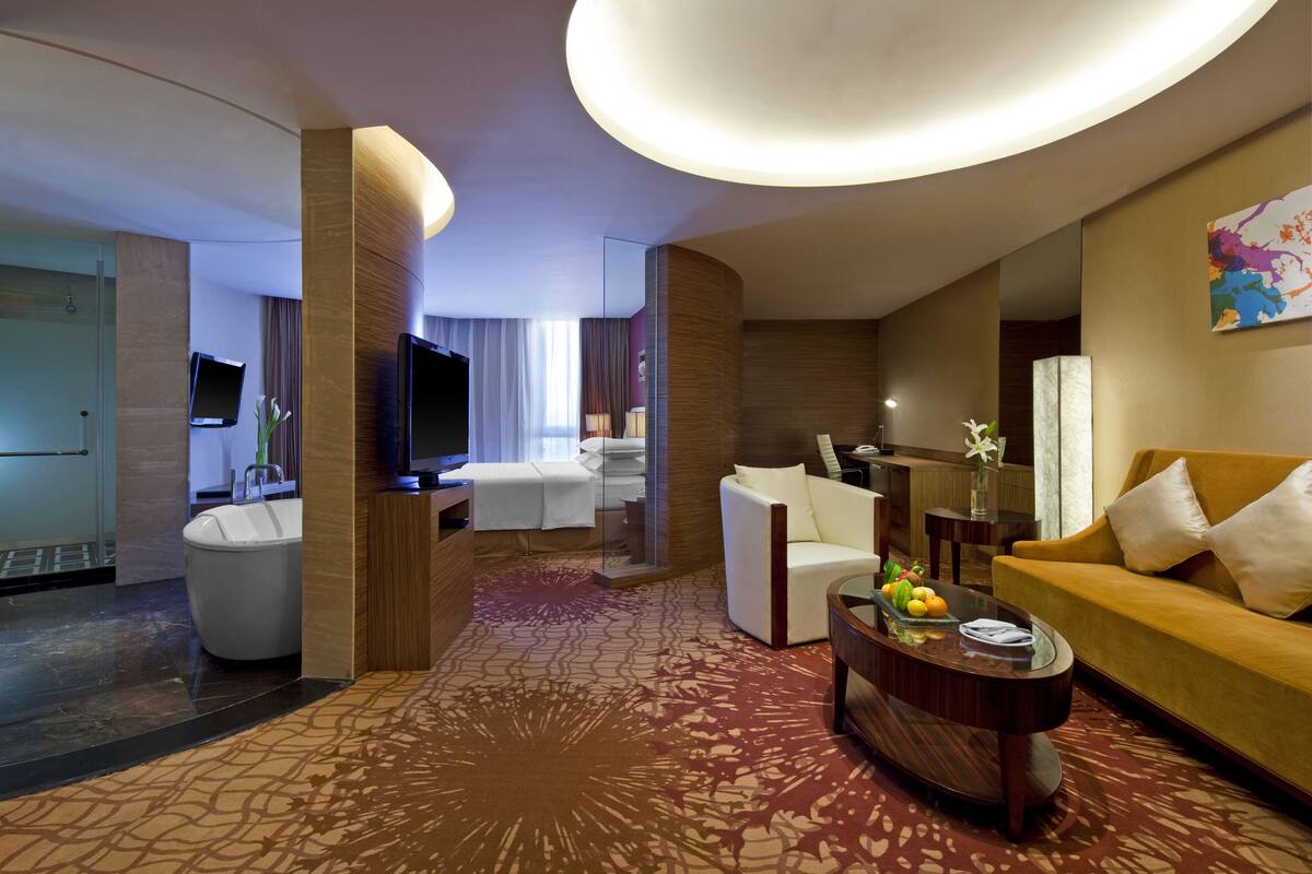 Una habitación de hotel moderna con sala de estar, bañera, sofá y televisor.
