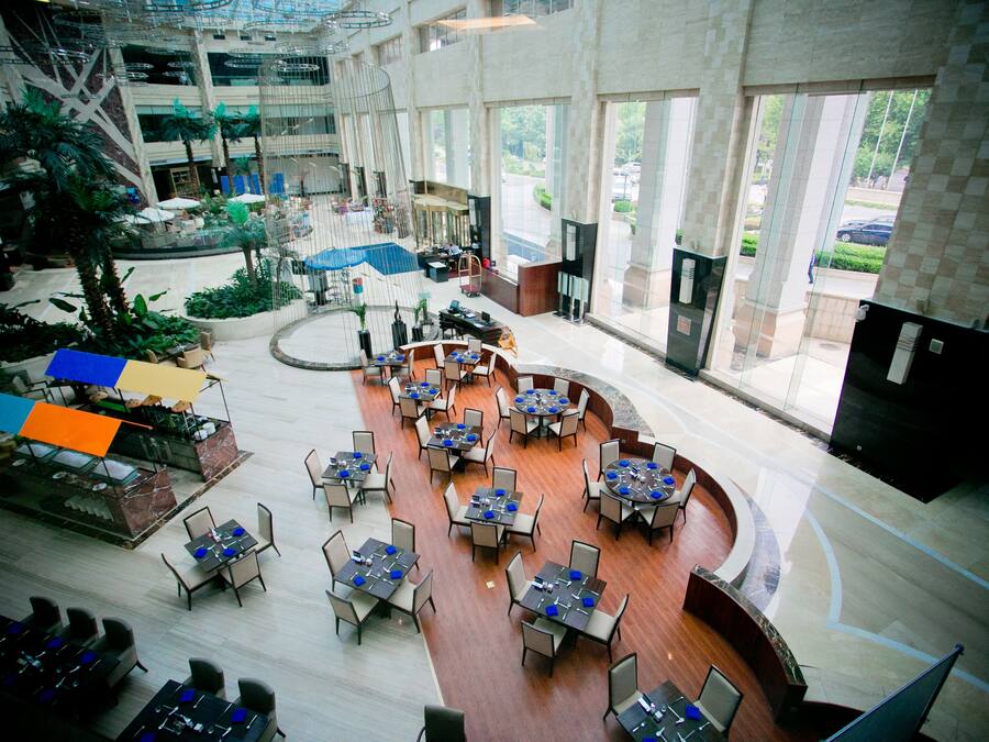 Un amplio espacio interior con varias mesas y sillas de comedor, una zona de estar central y grandes ventanales que ofrecen vistas al exterior.