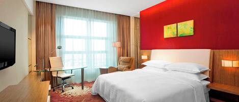 A hotel room with a large bed, a desk with a chair, a TV, and a window with curtains.
