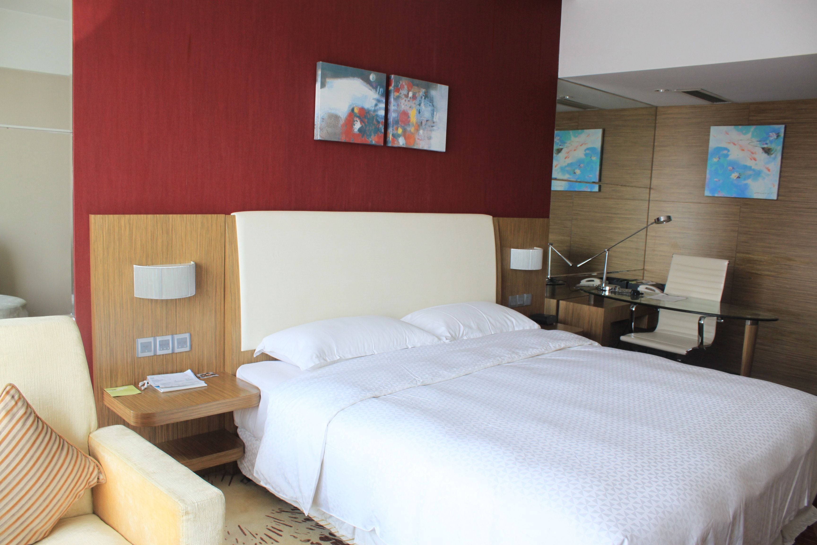 Habitación de hotel con una cama grande, cabecera de madera, mesita de noche con lámpara y dos cuadros en la pared.