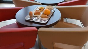 Un espace détente avec des tables et des chaises rondes, un plateau contenant de la nourriture et des boissons, et une vue sur l’extérieur par la fenêtre.