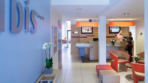 Un espace d’accueil d’hôtel au design moderne, comprenant un comptoir d’accueil, un coin salon et un panneau « bis » bien visible sur le mur.