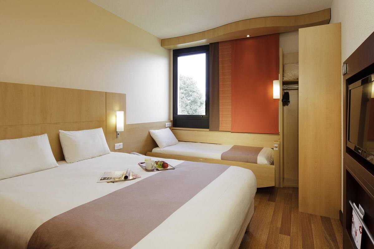 A hotel room with two beds, a TV, a window, and a door leading to a bathroom.