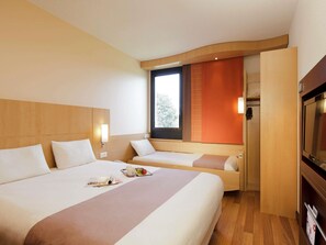 A hotel room with a large bed, a smaller bed, a TV, and a window with a view of trees.