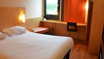 A hotel room with a bed, a desk, a chair, and a window with curtains.
