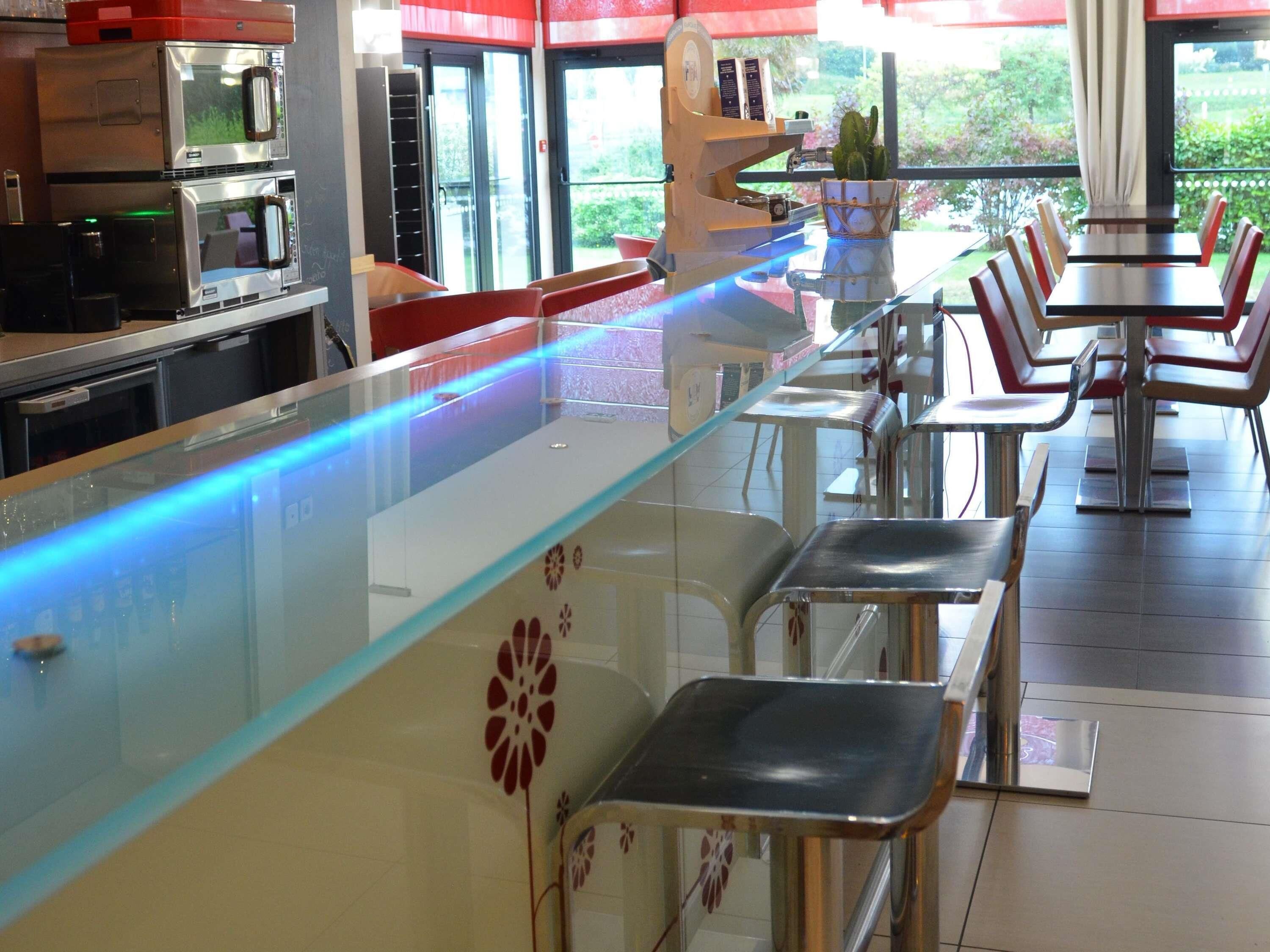 L’intérieur d’un restaurant avec un comptoir en verre, des chaises en métal et une vue sur la verdure à l’extérieur.