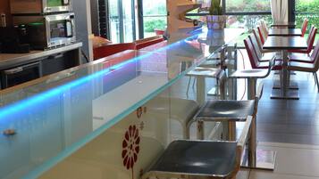 Un interior de restaurante con un mostrador de vidrio, sillas de metal y vistas a zonas verdes.