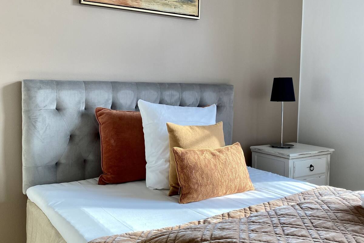 Un dormitorio con cabecera capitonada, una cama con cubrecama acolchado marrón y una mesita de noche con lámpara.