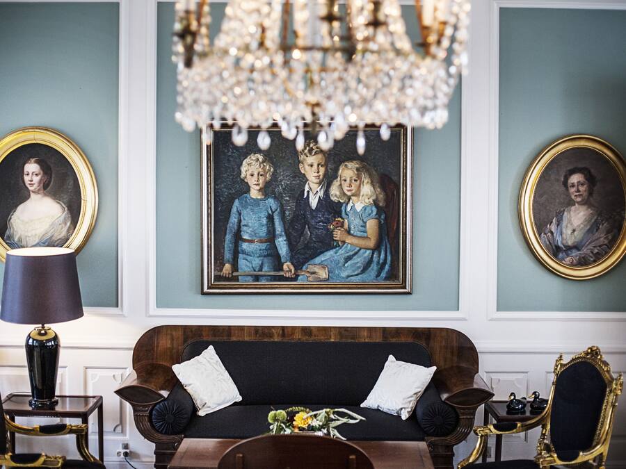 Una habitación con un sofá azul oscuro, una araña de cristal y retratos enmarcados en las paredes.