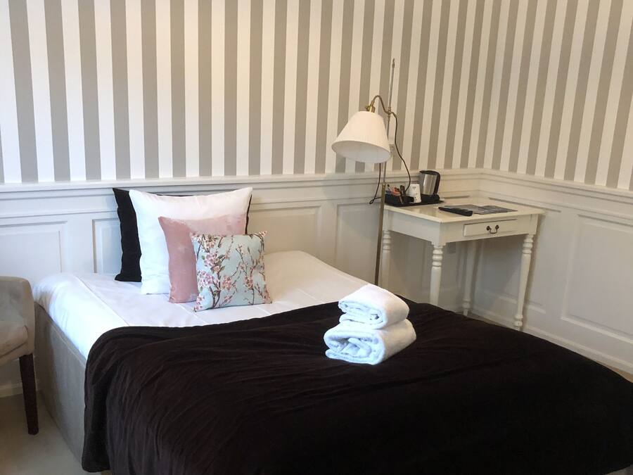 A neatly made bed with a black bedspread and white pillows, a bedside lamp, and a small white nightstand with a lamp.