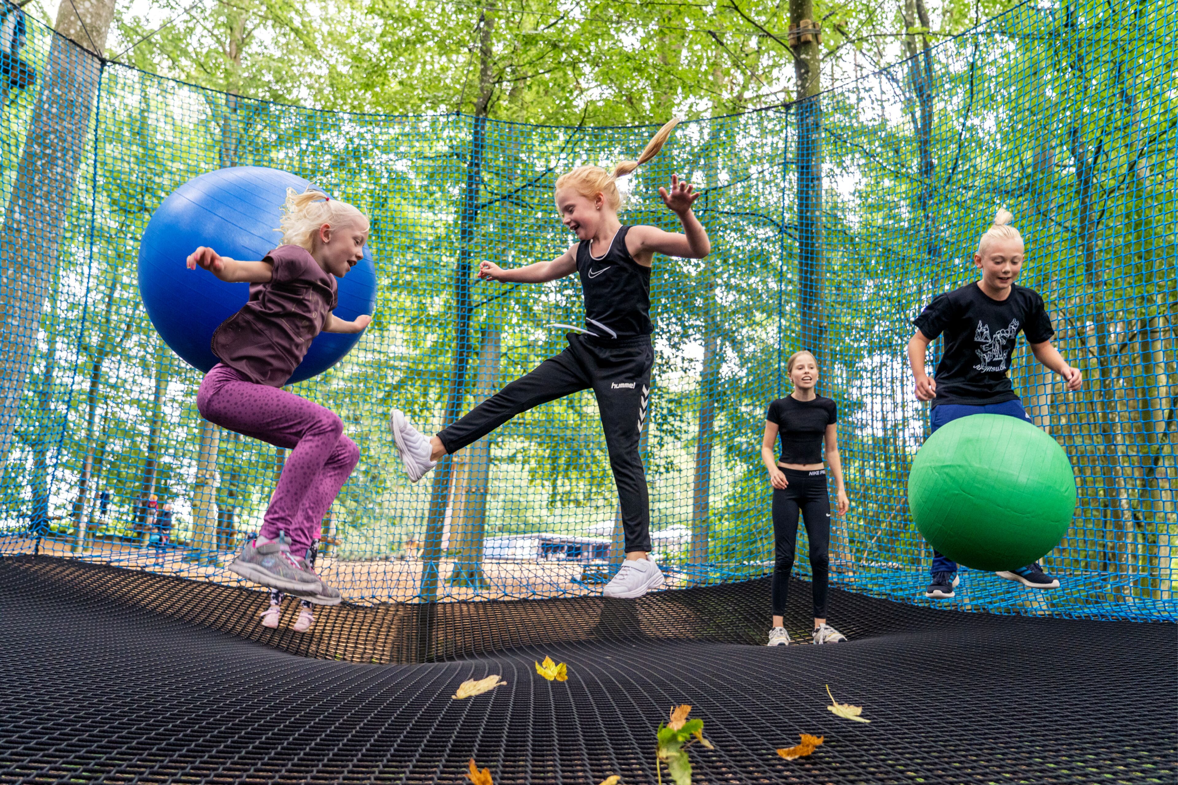 Un grupo de personas haciendo ejercicio en un trampolín dentro de un área exterior con red.