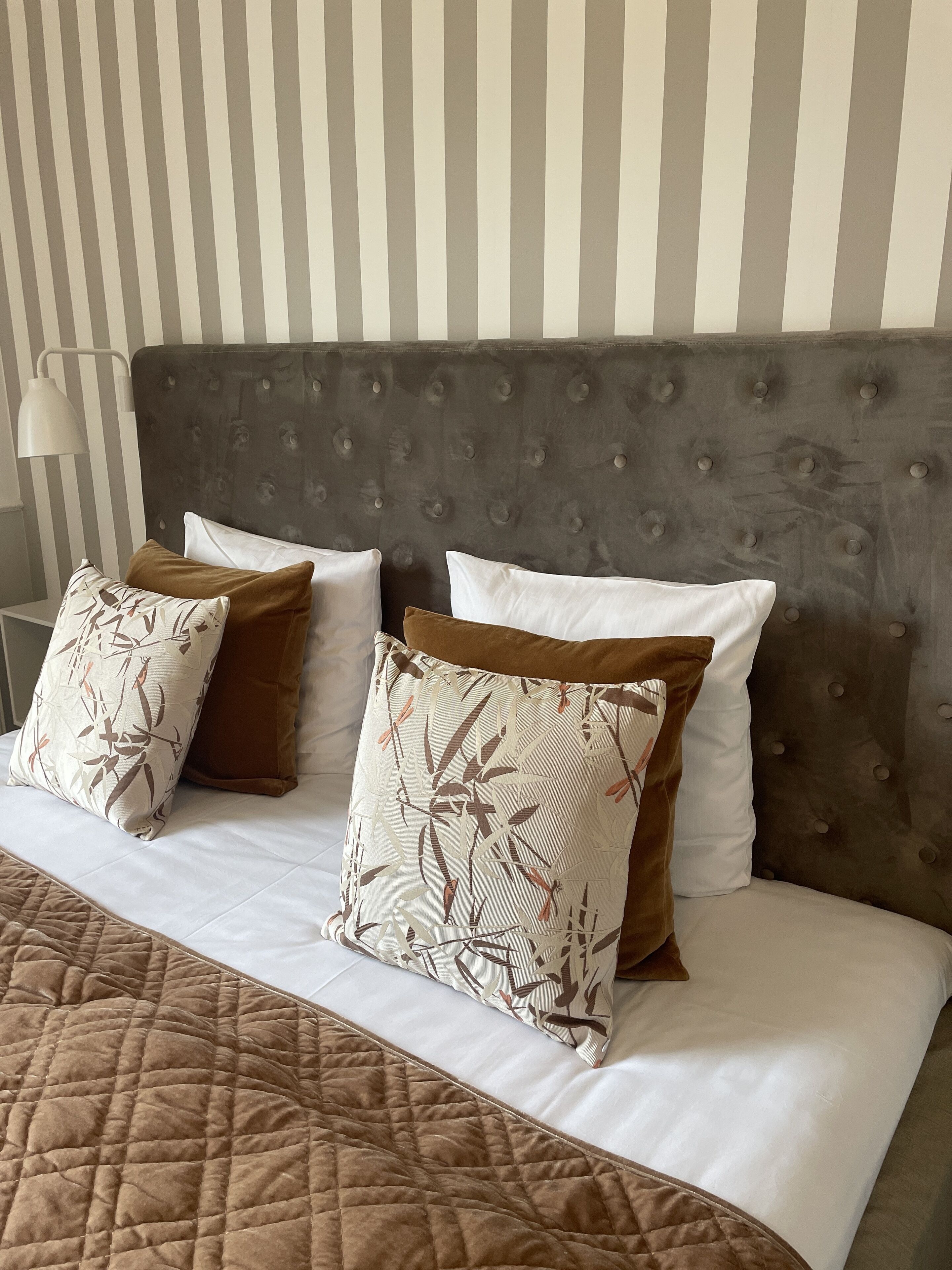 A neatly made bed with a quilted brown blanket, two pillows with a bamboo pattern, and a tufted headboard.