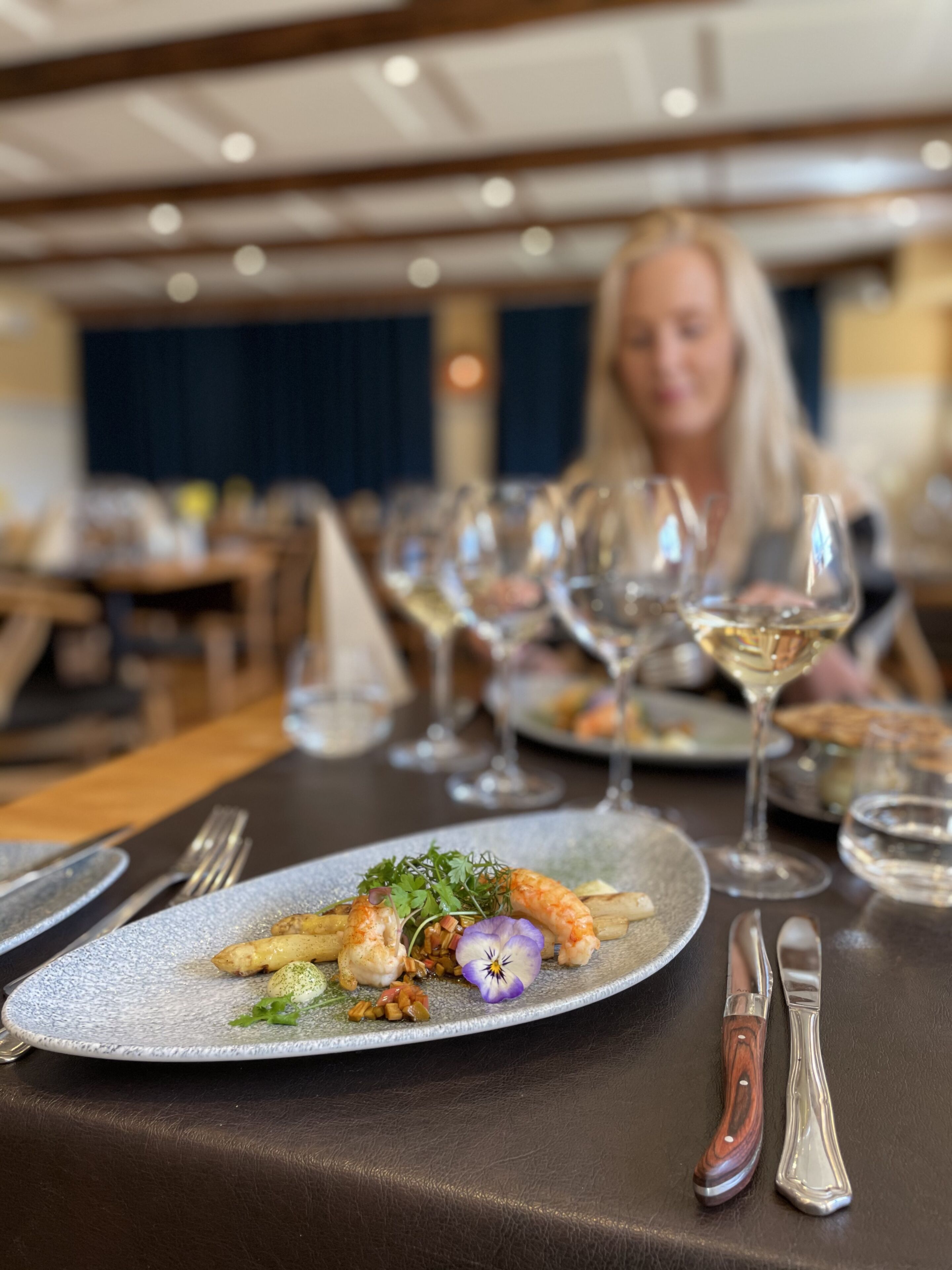 A dining table with plates of food, wine glasses, and cutlery.