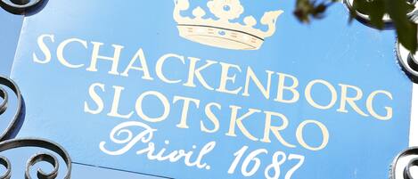 A sign with the text "SCHACKENBORG SLOTSKRO Privil. 1687" and a crown symbol.