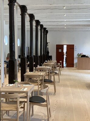 Un restaurante con mesas y sillas de madera, pilares oscuros y una barra de madera.