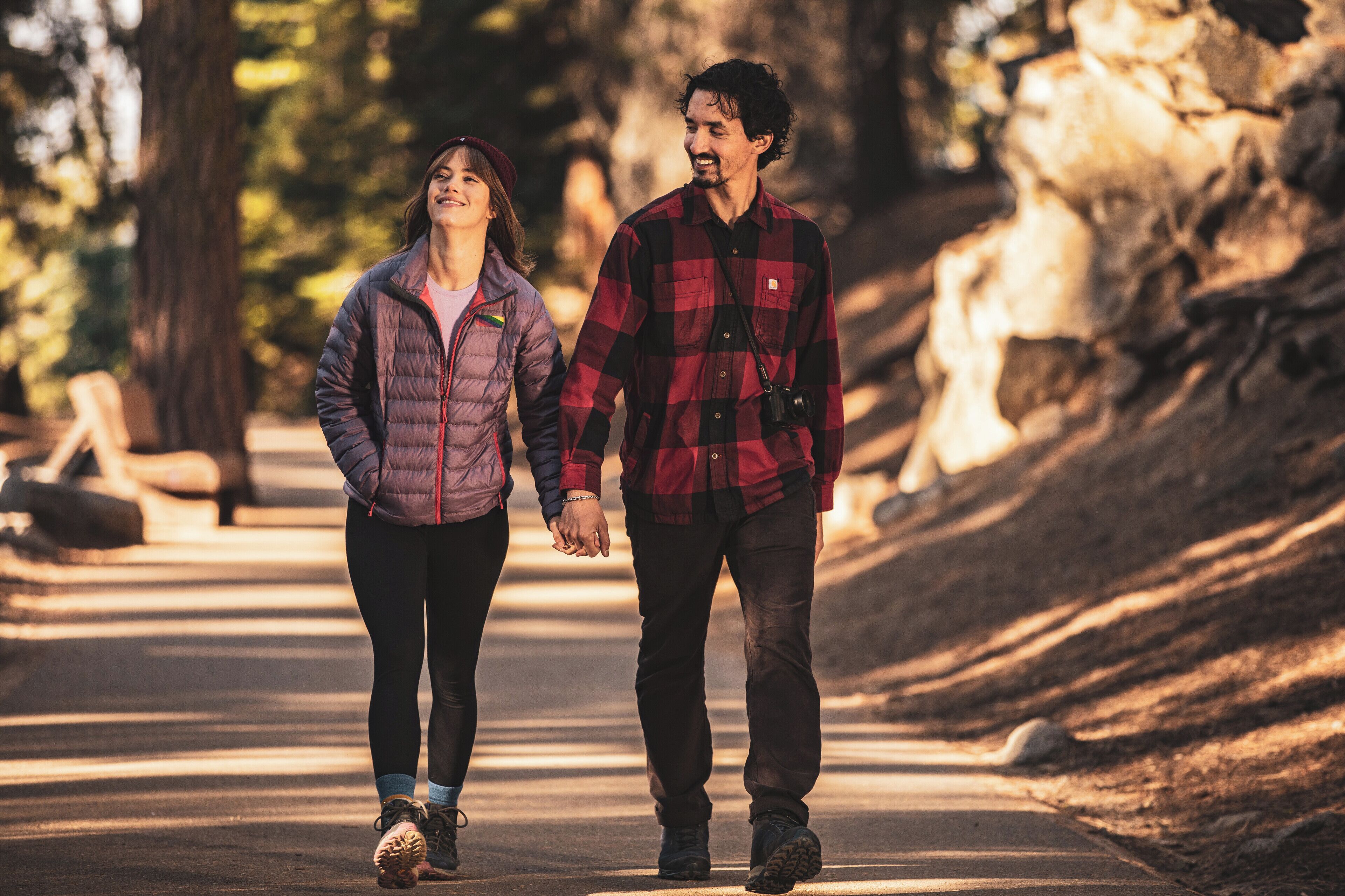 A couple walking on a paved path in a park with trees and rocks in the background.